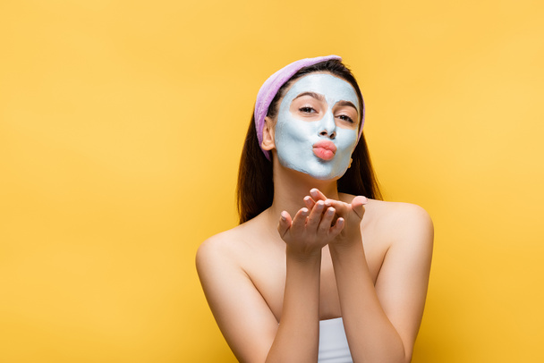 beautiful woman with clay mask on face blowing kiss isolated on yellow - Фото, зображення