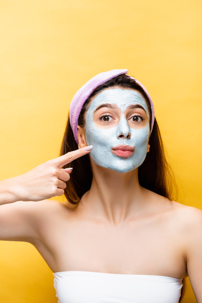 beautiful woman pointing at clay mask on face isolated on yellow - Фото, зображення