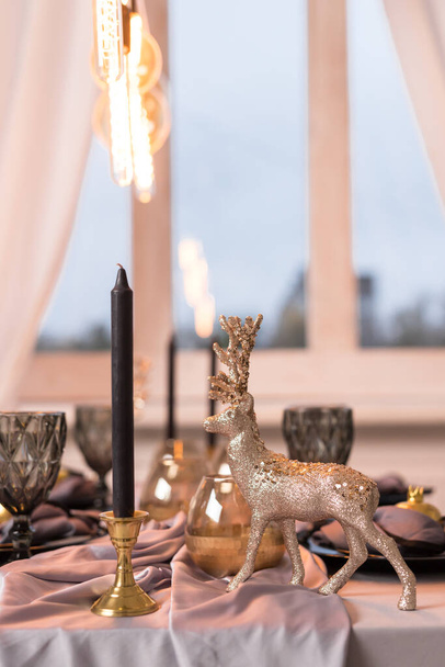 Detailní záběr slavnostního Vánočního stolku s prázdnými sklenicemi na víno a černým talířem se zlatým jelenem. Koncept Vánoc a Nový rok - Fotografie, Obrázek