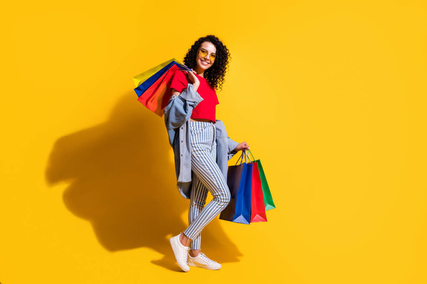 Profile photo of lady look camera hold shop packets wear red t-shirt striped jeans jacket sunglass sneakers isolated yellow color background - Фото, зображення