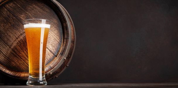 Een glas licht bier en een oud houten vat. met kopieerruimte - Foto, afbeelding