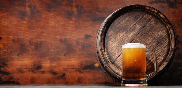 Mug of light lager beer and old wooden barrel. With copy space - Photo, Image