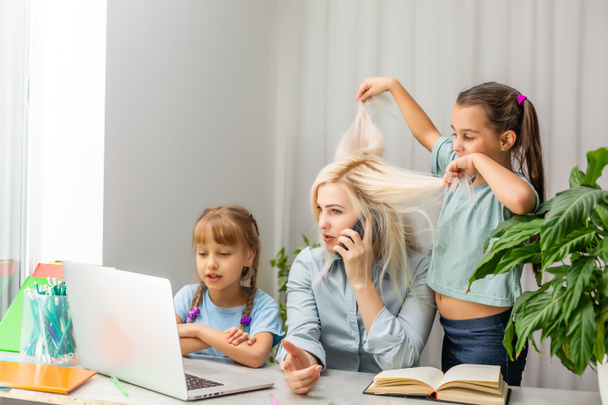A young mother with two children works from home on a computer. Fatigue Lifestyle Housewife Freelance. tired mother and two little daughters - 写真・画像