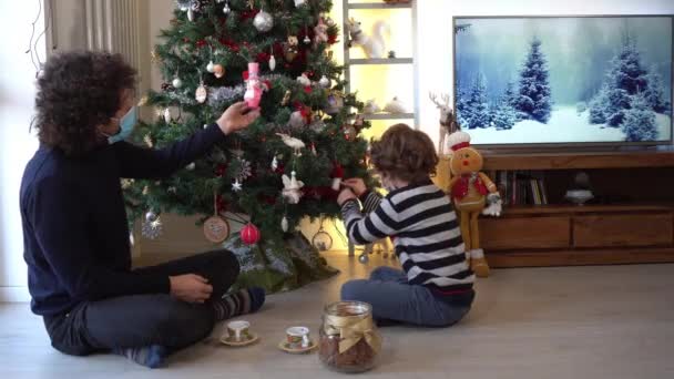 Άντρας με μικρό αγόρι με μάσκες κάθεται στο χριστουγεννιάτικο δέντρο στο σπίτι - Πλάνα, βίντεο