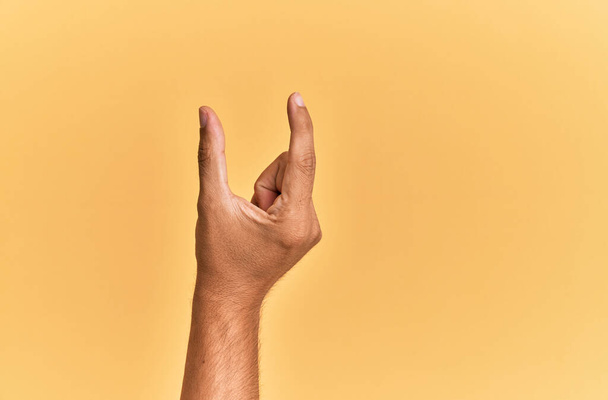 Braço e mão do homem caucasiano sobre amarelo isolado colhendo fundo e tomando coisa invisível, segurando objeto com os dedos mostrando espaço  - Foto, Imagem