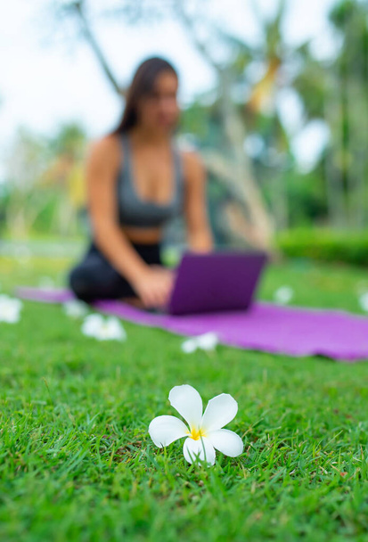 Flower Frangipani and blurry beautiful and athletic young woman trainer-instructor gives lessons through laptop remotely on the background - Photo, Image