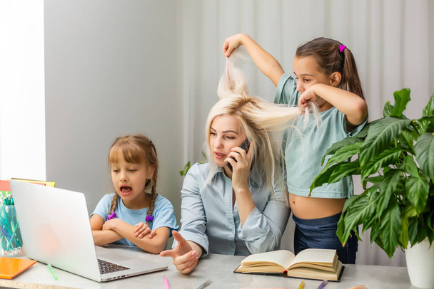 tired mother working at laptop and two little daughters playing - Фото, изображение