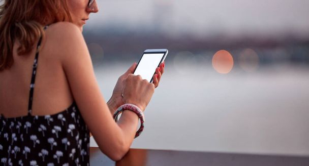 Mujer joven sosteniendo teléfono celular con pantalla blanca en blanco en el entorno urbano de la ciudad. - Foto, imagen
