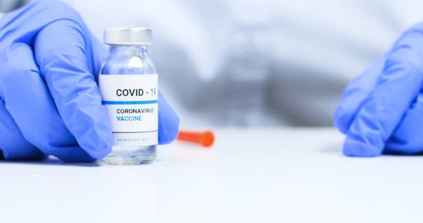Coronavirus-Impfstoff-Konzept. Nahaufnahme von Arzthänden in blauen medizinischen Handschuhen, die eine Spritze mit flüssigen Impfstoffen für Kinder oder ältere Erwachsene halten - Foto, Bild