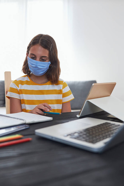 Meisje met medisch masker thuis leren tijdens viruspandemie en schoolbeperkingen. - Foto, afbeelding