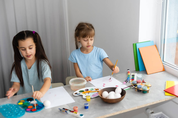 две счастливые милые девочки сестры рисовать пасхальные яйца, о смех, показать яйца и окрашенные руки - Фото, изображение
