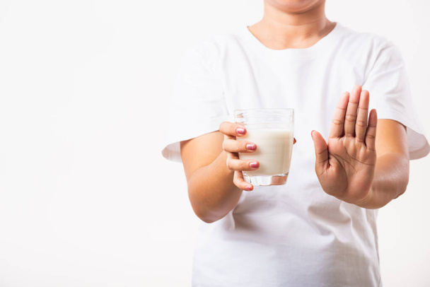 Closeup woman raises a hand to stop sign use hand holding glass milk she is bad stomach ache has bad lactose intolerance unhealthy problem with dairy food, studio shot isolated on white background - Photo, image