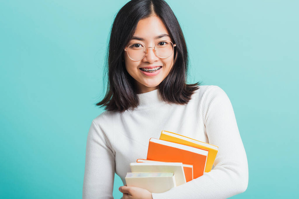 Portrait female in glasses is holding the books on hand, Young beautiful Asian woman hugging books, studio shot isolated on a blue background, Education concept - Foto, Imagem