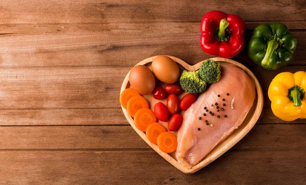 Top view of Raw chicken breasts fillets no boneless with spices rosemary, carrot, and eggs in heart plate wood on wooden background, Healthy food day concept - Photo, image