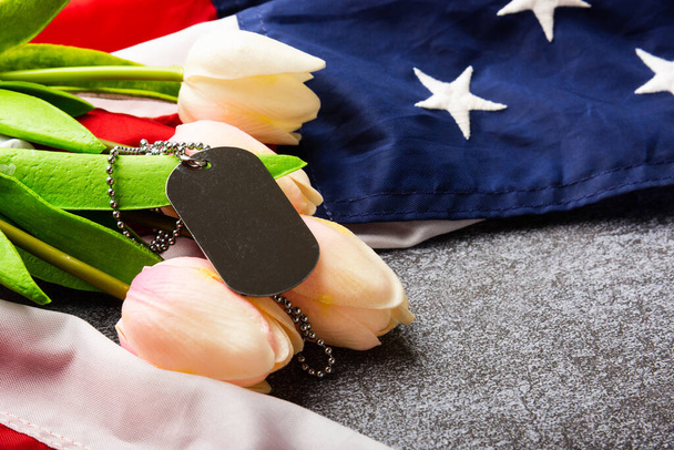 America United States flag and chain dog tags and tulip flower, military symbolizing, studio shot on concrete board background, US Veterans or Independence day concept - Фото, зображення