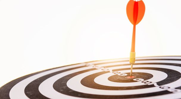 Dart arrow hitting to center on bullseye (bull's-eye) dartboard is the target of purpose challenge business at sunset, expert marketing strategy target, objective financial and goal success - Foto, imagen