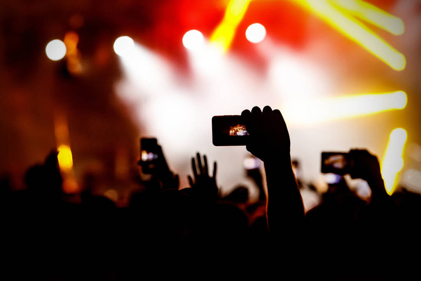 Kéz sziluettje kamerás telefonnal élő koncerten képeket és videókat készít. - Fotó, kép