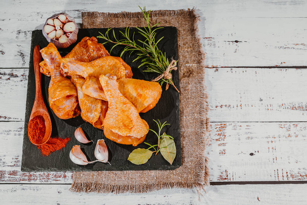 Chicken drumstick marinated in plates on a wooden background with wooden spoons and spices. - Fotografie, Obrázek