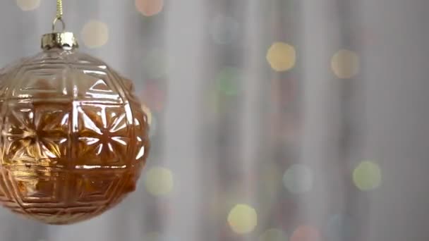 Bonito brinquedo de árvore de Natal pendura no fundo de luzes de Natal multi-coloridas e se move ligeiramente. Close-up. Brinquedo de árvore de Natal na forma de uma esfera, transparente. - Filmagem, Vídeo
