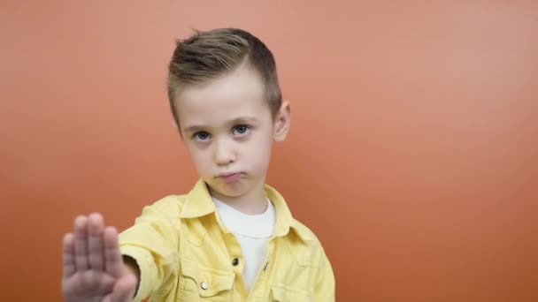 Serious young kid waving finger no hand sign look at camera isolated orange background - Footage, Video