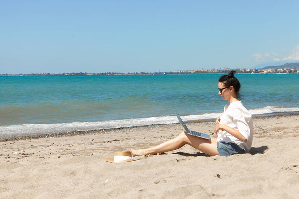 Young woman using laptop computer on a beach. Vacation lifestyle communication. Freelance work concept - Photo, Image