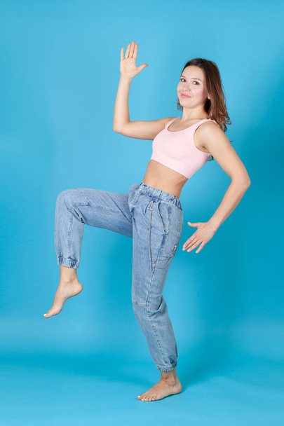 a full length young woman in jeans dances like Pinocchio isolated on a blue background - Фото, зображення