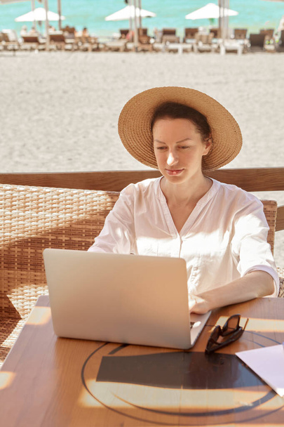 Kumsalda dizüstü bilgisayar kullanan genç bir kadın. Serbest çalışma kavramı - Fotoğraf, Görsel