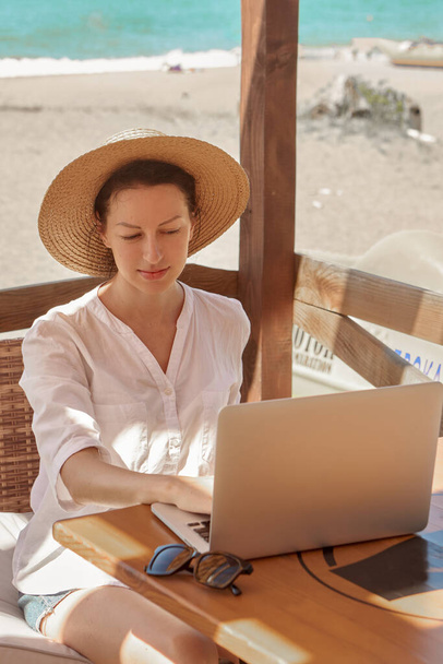 ビーチでラップトップコンピュータを使用している若い女性。フリーランスの仕事のコンセプト - 写真・画像