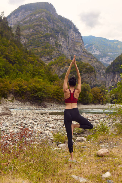 Cours de yoga dans la nature. Une femme fait du yoga dans les montagnes, près d'une rivière de montagne coule. Le concept de faire du sport seul. Exclusion sociale - Photo, image