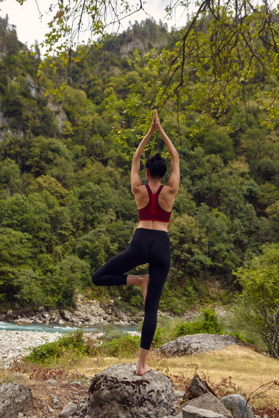 Yoga lessen in de natuur. Het concept van alleen sporten. Sociale uitsluiting. Een vrouw doet yoga op rotsen, vlakbij een bergrivier stroomt - Foto, afbeelding
