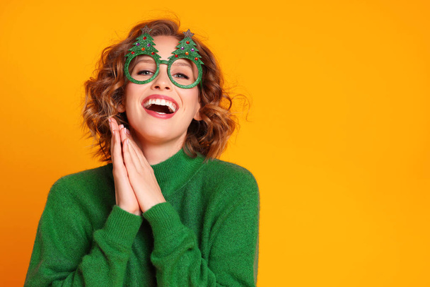 divertida mujer joven alegre en gafas tontas con árboles de Navidad riendo y divirtiéndose en un fondo amarillo brillante - Foto, Imagen