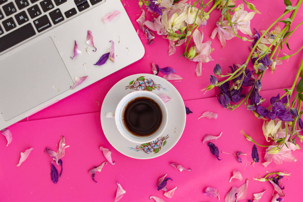 Escritorio de la oficina. Espacio de trabajo femenino con portátil y taza de café, flores y pétalos sobre fondo rosa. Asiento plano, vista superior. Mirada del blog de moda. Añadir su texto. - Foto, Imagen