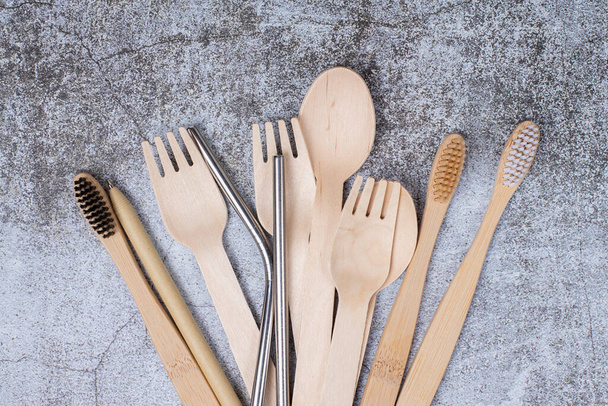 Basic set eco friendly reusable bamboo cutlery, toothbrushes, metal tubes on gray background close up. Concept of environmental protection, plastic free, zero waste. Minimalistic life - Фото, изображение