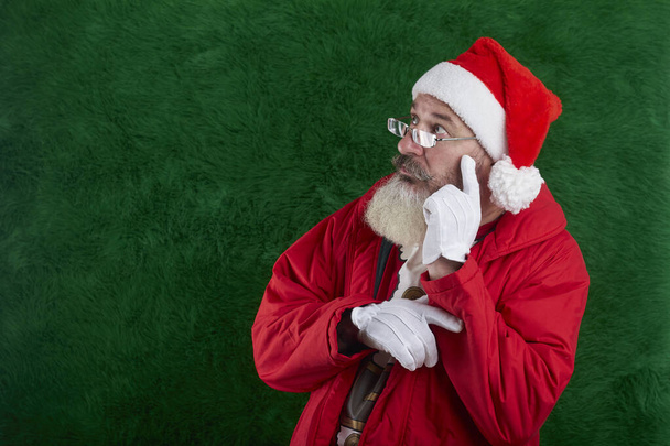 Mature bearded man with eyeglasses on face wearing Santa hat, Santa looks away at something, copy space - Fotografie, Obrázek