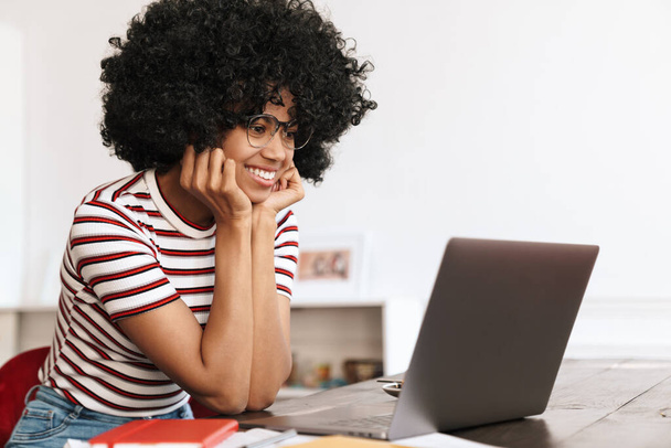 Smiling african american student girl doing homework with laptop while sitting in cafe - Photo, image