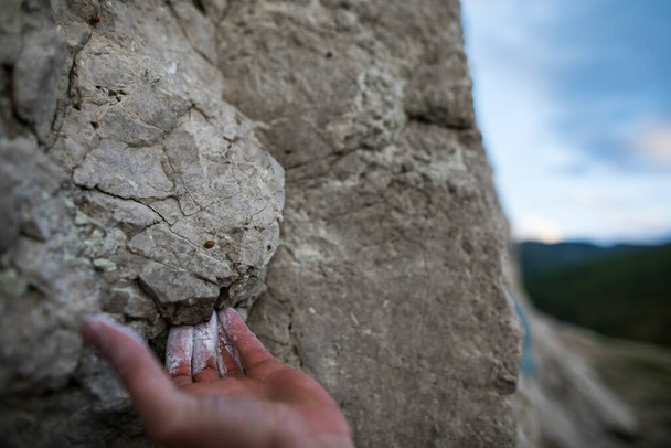 Κοντινό πλάνο ενός ενήλικου άνδρα που κρατιέται από ένα βράχο, εικονογράφηση για αναρρίχηση σε βράχο. - Φωτογραφία, εικόνα