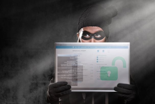 サイバー犯罪とハッキングの概念。パスワードウィンドウで透明なタブレットを保持している黒の帽子、手袋、マスク、中の女性の肖像画。暗い背景。スペースのコピー. - 写真・画像