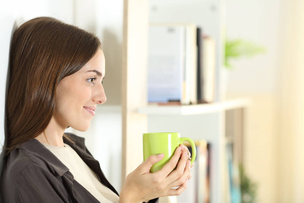 Side view portrait of a satisfied woman holding coffee mug contemplating at home - Photo, Image