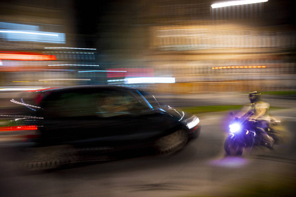 Bir motosikletçi ve hareket hâlindeki bir araba ile tehlikeli şehir trafiği durumu. Odaklanmamış resim - Fotoğraf, Görsel