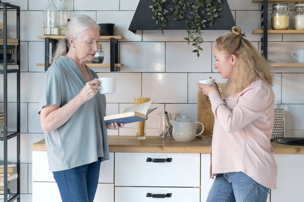 Barátságos családi képek nézegetése otthon. Az idősebb nő élvezi, hogy beszélgethet a lányával. Egy csésze teát isznak a konyhában. Idős nő női gondozóval a nappaliban - Fotó, kép