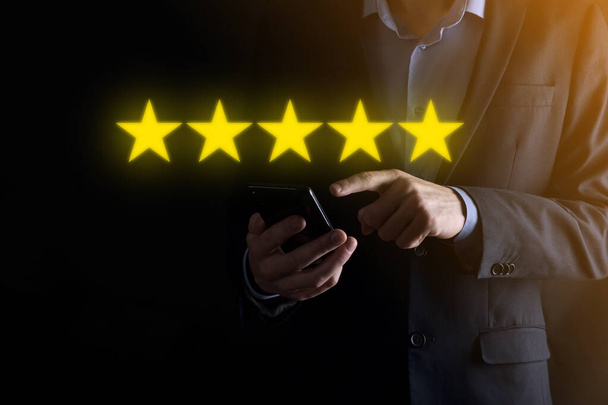 Man Hand Smartphone zeigt auf fünf Sterne ausgezeichnete Bewertung.Zeigen fünf Sterne Symbol, um die Bewertung des Unternehmens zu erhöhen.Bewertung, Erhöhung der Bewertung oder des Rankings, Bewertung und Klassifizierungskonzept - Foto, Bild