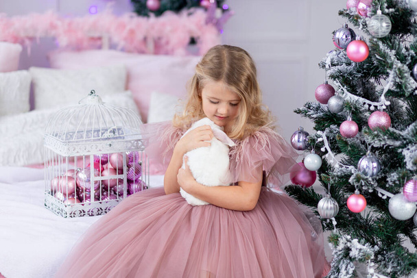 Маленька дівчинка з кроликом на ялинці в красивій рожевій сукні, новий рік і Різдво концепції - Фото, зображення