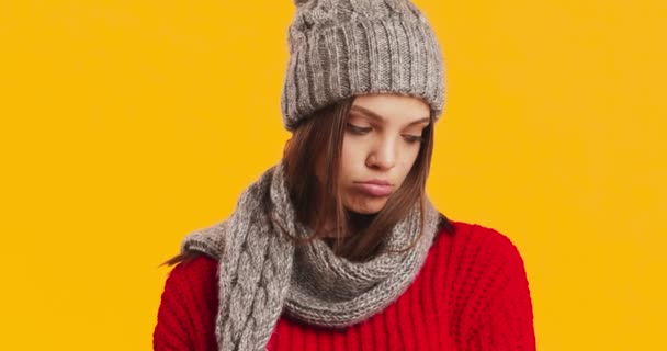 Close up retrato de triste jovem mulher vestindo chapéu e cachecol de inverno, lábios amuados, fundo estúdio laranja - Filmagem, Vídeo