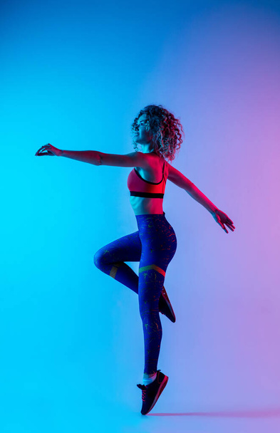 Young sportive woman training isolated on gradient pink-blue studio background in neon light. - 写真・画像