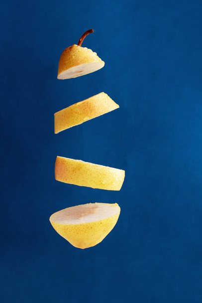 zwevende stukjes gele peer tegen een blauwe achtergrond, creatief plaatje - Foto, afbeelding