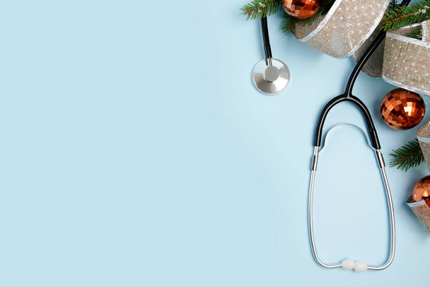 Lékařské Vánoce a Nový rok. Stethoscope a zlaté vánoční strom koule na modrém pozadí s kopírovacím prostorem - Fotografie, Obrázek