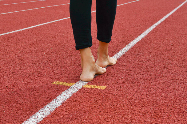 陸上競技場のレーンの斜めの白い線の上を歩いているときに黒い足と裸の足を持つ者 - 写真・画像