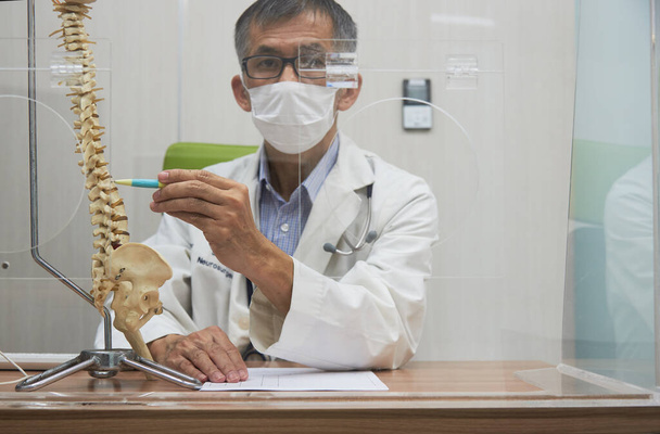 Νευροχειρουργός που χρησιμοποιεί πένα δείχνοντας το μοντέλο της ανθρώπινης σπονδυλικής στήλης στο ιατρικό γραφείο κατά τη διάρκεια πανδημίας covid-19 - Φωτογραφία, εικόνα