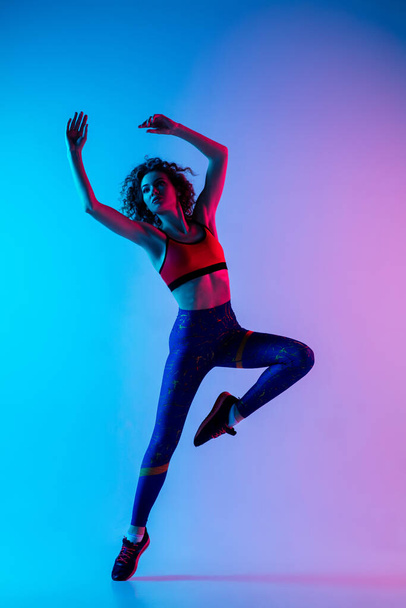 Portrait of young beautiful woman in bright sportwear isolated on gradient pink-blue studio background in neon light. - 写真・画像