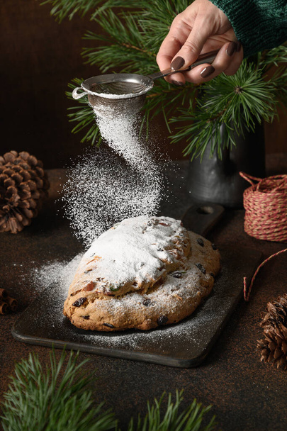 Woman powdered sugar Christmas stollen on brown background. Holiday pastry dessert. Vertical format. Close up. - Foto, Bild
